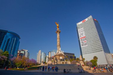 Mexico City, Meksika - 14 Mart 2022: Güneşli bir bahar gününde Özgürlük Anıtı ve döner kavşak, modern binalar ve arka planda çiçek açan Jacaranda ağaçları