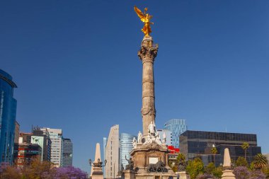 Mexico City, Meksika - 14 Mart 2022: Güneşli bir bahar gününde Özgürlük Anıtı ve döner kavşak, modern binalar ve arka planda çiçek açan Jacaranda ağaçları