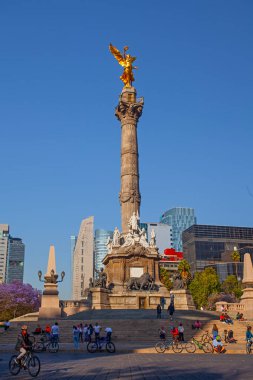 Mexico City, Meksika - 14 Mart 2022: Güneşli bir bahar gününde Özgürlük Anıtı ve döner kavşak, modern binalar ve arka planda çiçek açan Jacaranda ağaçları