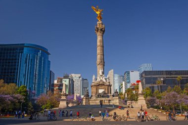Mexico City, Meksika - 14 Mart 2022: Güneşli bir bahar gününde Özgürlük Anıtı ve döner kavşak, modern binalar ve arka planda çiçek açan Jacaranda ağaçları