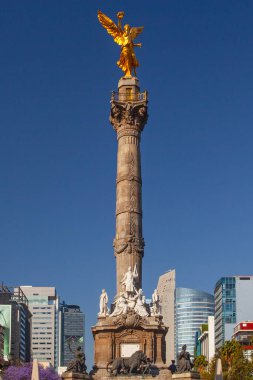 Mexico City, Meksika - 14 Mart 2022: Güneşli bir bahar gününde Özgürlük Anıtı ve döner kavşak, modern binalar ve arka planda çiçek açan Jacaranda ağaçları