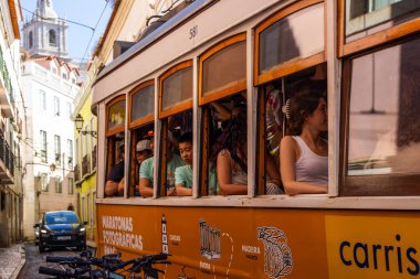 Lizbon, Portekiz - 27 Temmuz 2025: Klasik bir ünlü sarı tramvay Lizbon 'daki canlı kırmızı tarihi binalardan sabah erken saatlerde geçiyor