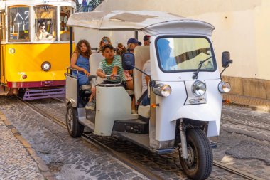 Lizbon, Portekiz - 27 Temmuz 2025: Klasik bir ünlü sarı tramvay Lizbon 'daki canlı kırmızı tarihi binalardan sabah erken saatlerde geçiyor