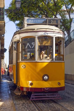 Lizbon, Portekiz - 27 Temmuz 2025: Klasik bir ünlü sarı tramvay Lizbon 'daki canlı kırmızı tarihi binalardan sabah erken saatlerde geçiyor