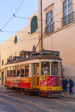 Lizbon, Portekiz - 27 Temmuz 2025: Klasik bir ünlü sarı tramvay Lizbon 'daki canlı kırmızı tarihi binalardan sabah erken saatlerde geçiyor