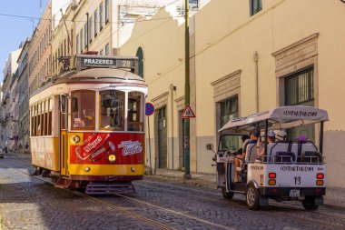Lizbon, Portekiz - 27 Temmuz 2025: Klasik bir ünlü sarı tramvay Lizbon 'daki canlı kırmızı tarihi binalardan sabah erken saatlerde geçiyor