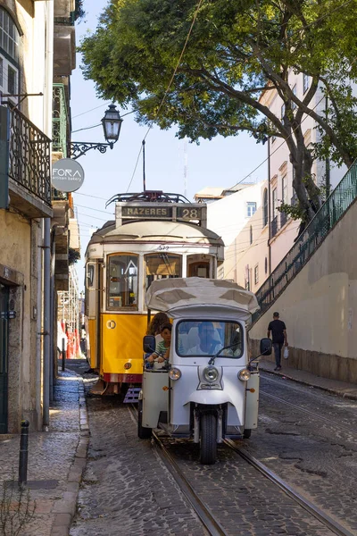 Lizbon, Portekiz - 27 Temmuz 2025: Klasik bir ünlü sarı tramvay Lizbon 'daki canlı kırmızı tarihi binalardan sabah erken saatlerde geçiyor