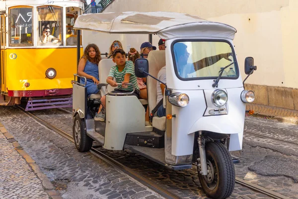 Lizbon, Portekiz - 27 Temmuz 2025: Klasik bir ünlü sarı tramvay Lizbon 'daki canlı kırmızı tarihi binalardan sabah erken saatlerde geçiyor