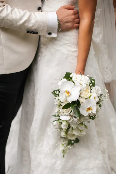 Groom hugs bride who is holding a bouquet — Stock Photo, Image