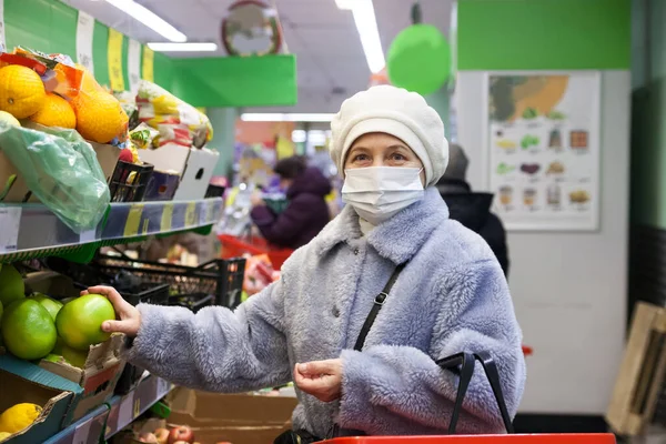 senior old woman shopping at the supermarket selects products in a medical mask. Pandemic coronavirus covid 19