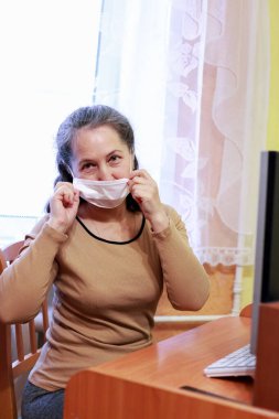 Yüz maskesi takan yaşlı bir kadın bilgisayar başında çalışıyor.
