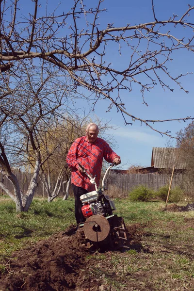 Elderly farmer with cultivator working in village garden