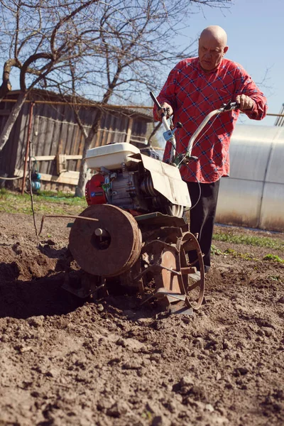 Elderly farmer with cultivator working in village garden