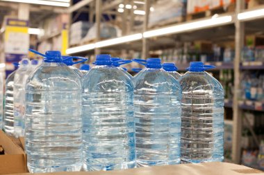 Süpermarkette temiz içme suyu olan mavi kapaklı plastik şişeler. Plastik ambalajla paketlenmiş