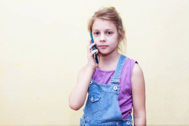 8 yaşındaki bir kız akıllı telefondan konuşuyor. Sarı arkaplan