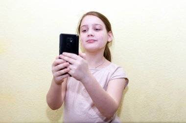 10 yaşında bir kız akıllı telefon ekranına bakıyor. Sarı sırtı