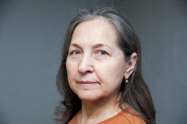 Duvarın gri arka planında yalnız duran olgun kadın.