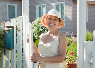  Güzel, şapkalı yaşlı bir kadın bir kır evinin kapısında duruyor.