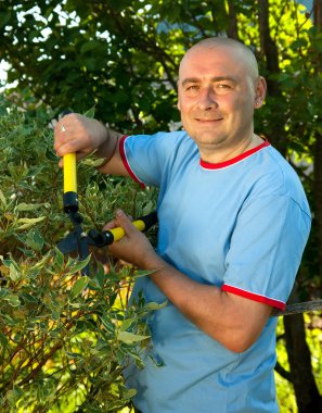 Erkek bahçıvan, çalıların yanında budama makinesi var. 