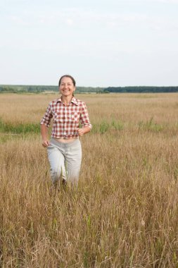 Olgun bir kadın yaz manzarasında koşuyor.