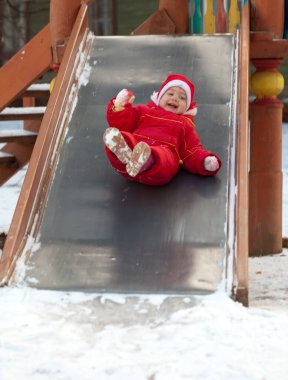 Küçük kız kışın oyun parkında kayıyor.