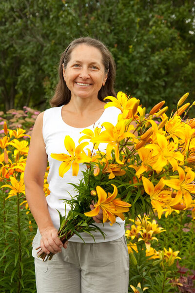 Mature gardener  in flower bed with bouguet of orange lilies