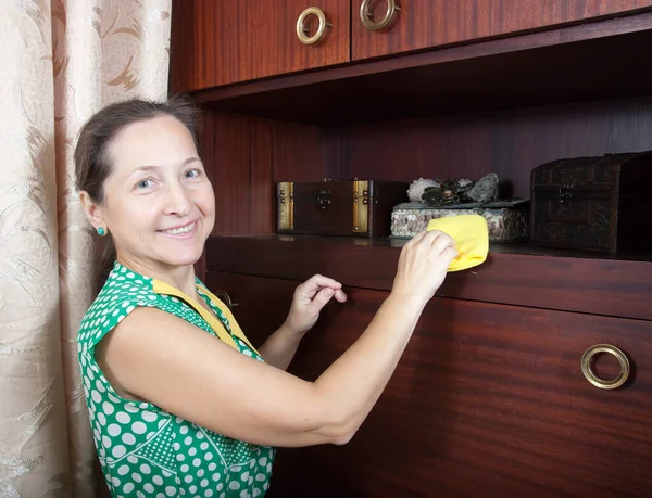 Mature woman cleans a furniture indoor