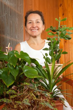  Evde saksıda çiçek tutan olgun bir kadın.