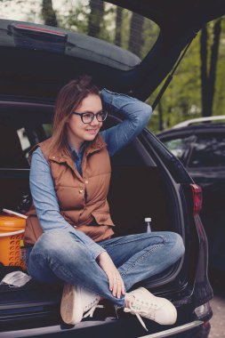 Otoparktaki off-road aracının açık bagajında mutlu sarışın kadın.  