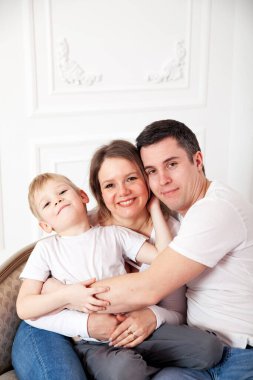 Beyaz elbiseli bir aile ve beyaz duvarda açık renkli bir kanepe.