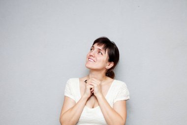 Beyaz elbiseli kadın gri arka planda poz veriyor.