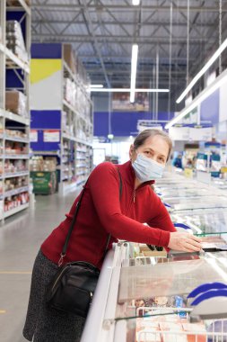 Süpermarkette kıdemli bayan müşteri koruyucu tıbbi maske takıyor.