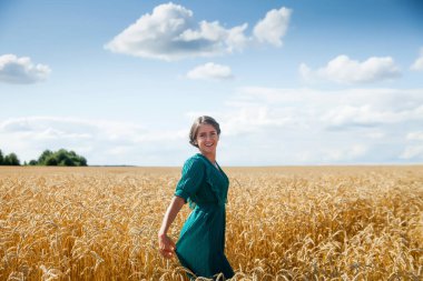 Portrait of   beautiful long-haired girl in   green dress in   wheat fiel