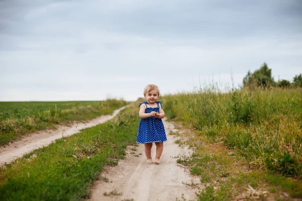 1岁的小女孩穿着蓝色的太阳衣沿着乡间小路跑着 — 图库照片