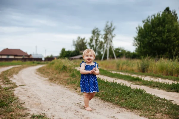 穿着蓝色太阳衣的小女孩沿着乡间小路跑着 — 图库照片