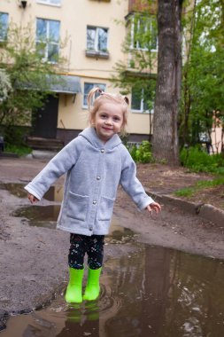 Su birikintilerinde zıplayan yeşil lastik çizmeli bebeğin bahar portresi. 