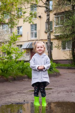 Lastik çizmeli küçük kız su birikintilerinde yürüyor.