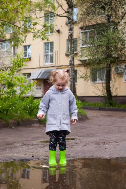 Su birikintilerinde zıplayan yeşil lastik çizmeli bebeğin bahar portresi. 