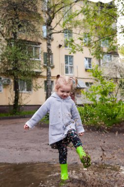 Lastik çizmeli küçük kız su birikintilerinde yürüyor.