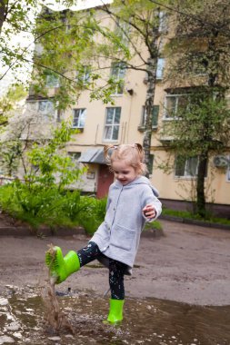 Lastik çizmeli küçük kız su birikintilerinde yürüyor.