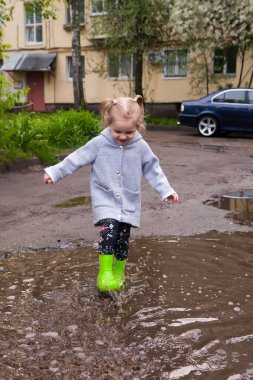Lastik çizmeli küçük kız su birikintilerinde yürüyor.