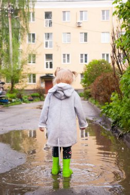 Yeşil lastik çizmeli bir bebeğin bahar portresi su birikintilerinde yürüyor.. 