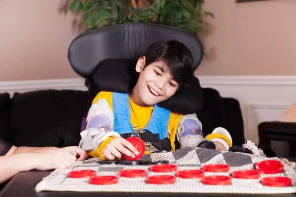 Kleiner behinderter Junge im Rollstuhl spielt Checker — Stockfoto