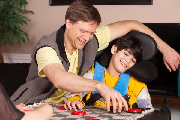 Disabled boy in wheelchair playing checkers with father at home — Stock Photo, Image