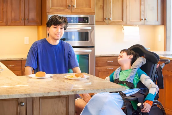 Niño discapacitado en silla de ruedas en la cocina con su hermano mayor —  Fotos de Stock