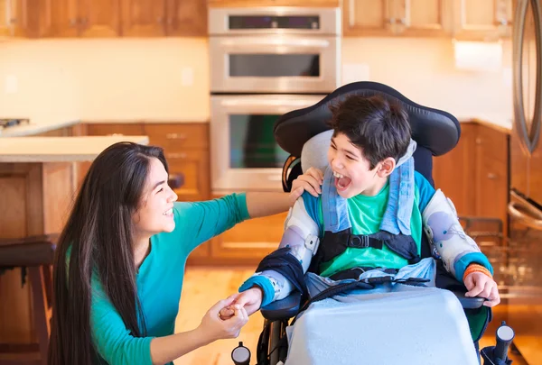 Garçon handicapé en fauteuil roulant riant avec soeur adolescente dans la cuisine — Photo