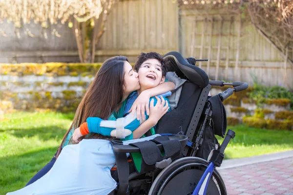 Schwester küsst und umarmt behinderten kleinen Bruder im Rollstuhl — Stockfoto