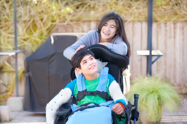 Nastolatek siostra dbanie o niepełnosprawnych brat na wózku inwalidzkim z — Zdjęcie stockowe