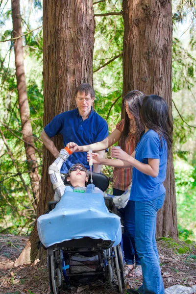 Famille tube alimentation garçon handicapé en fauteuil roulant à l'extérieur en bois — Photo