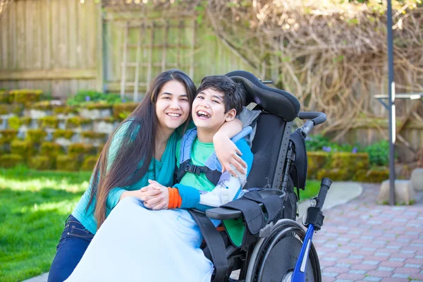 Teenage girl hugging disabled brother in wheelchair outdoors — Stock Photo, Image